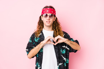 Young hippie caucasian man isolated smiling and showing a heart shape with hands.