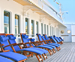 Wooden teak deck chairs and sun loungers with blue  pillows and upholstery on deck of luxury...