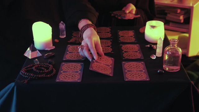 Medium shot of witchy hand putting Taro card on desk while fortune spelling