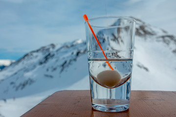 on a table stands a glass with alcohol and in the background are the snow-covered mountains