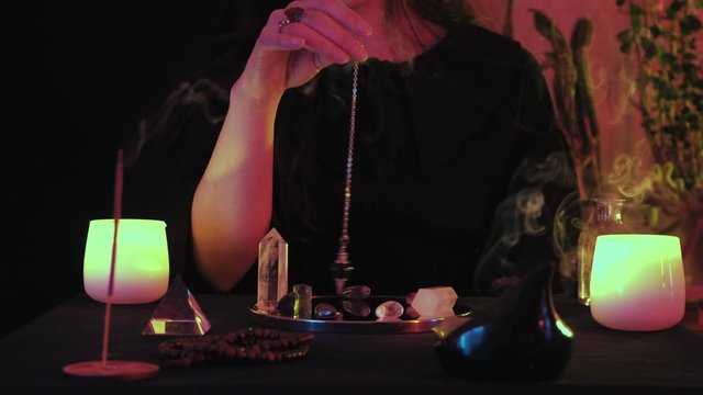 Medium close up of fortune spelling enchantress with pendulum