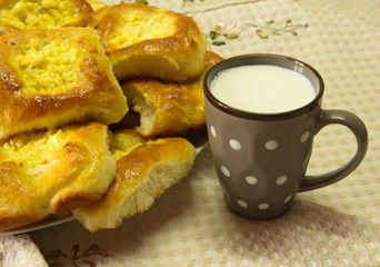  On a beige tablecloth there is a gray ceramic cup with milk and homemade cakes: fresh curd cheesecakes.