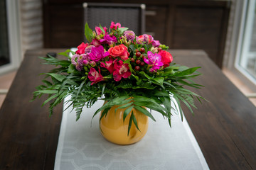 a brown table with a white tablecloth stands a colourful bouquet of flowers in a yellow vase