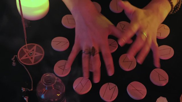 Medium top view shot of witchy hands mixes the runes before the fortune spelling