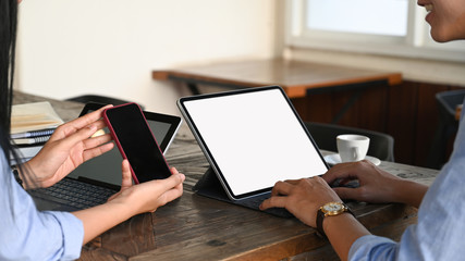 A woman showing black blank screen smartphone to A man who typing on white screen tablet. Collaboration concept.