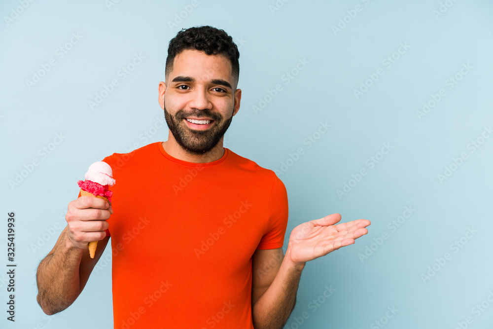 Wall mural young latin man holding an ice cream isolated showing a copy space on a palm and holding another han