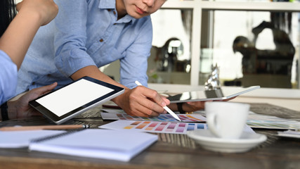 Cropped image of graphic designer discussing at the wooden meeting table with working stuff.