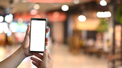 Hands holding a white blank screen smartphone with blurred background.