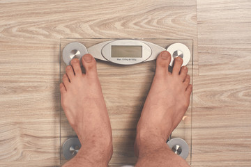 fat man on glass scales background wooden parquet. close up