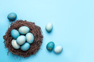 Easter eggs in nest on blue background. Flat lay, top view.
