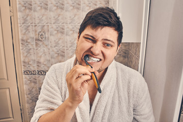 a man in a white coat is brushing his teeth in the bathroom.