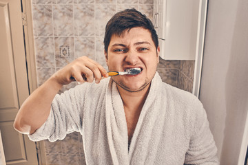 a man in a white coat is brushing his teeth in the bathroom.