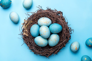 Easter eggs in nest on blue background. Flat lay, top view.