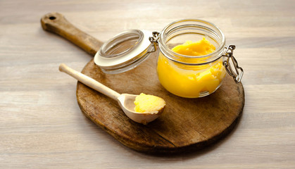 Ghee clarified butter desi in glass jar with spoon made from wood on natural wooden background
