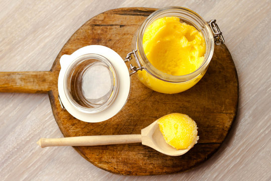 Ghee clarified butter desi in glass jar with spoon made from wood on natural wooden background