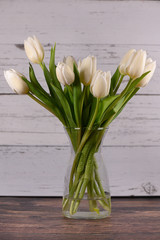 White tulip in clear vase on a dark wood base white wood background center of page 