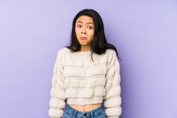Young chinese  woman isolated on a purple background shrugs shoulders and open eyes confused.