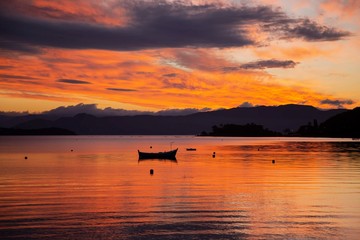 Naklejka premium Boat moored at the bay, Sambaqui beach. Colorful orange and red clouds. Florianópolis, Santa Catarina / Brazil