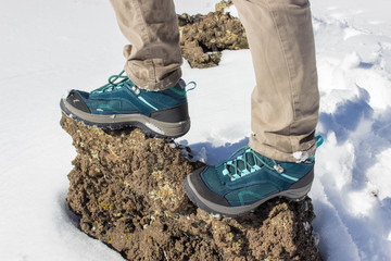 top view of trekking shoes on the lava stone and snow background, female legs.