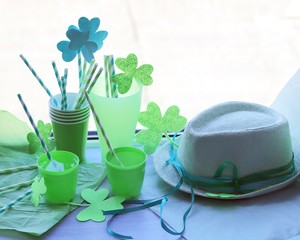 St. Patrick Day, glasses with a green drink, cocktail tubes with a decorative shamrock, clover on a wooden surface on a window background, getting ready for a party