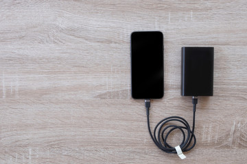 Smartphone charging with power bank on wood background.