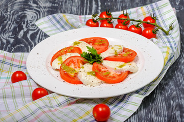 Snack from slices of tomatoes and mozzarella with pesto and herbs. Restaurant serving
