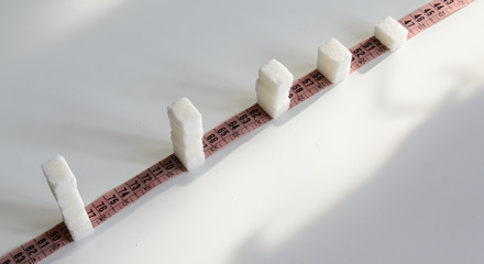 pieces of sugar on a measuring tape one, two, three. Concept - Excessive sugar intake leads to obesity and diabetes.