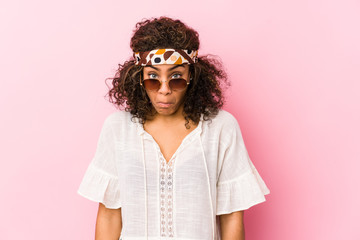 Young african american hipster woman isolated on pink background shrugs shoulders and open eyes confused.