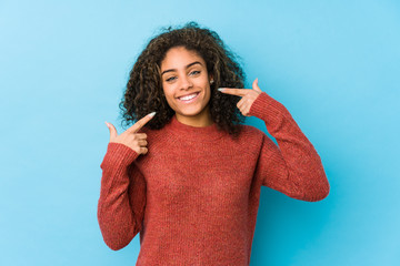 Young african american curly hair woman smiles, pointing fingers at mouth.