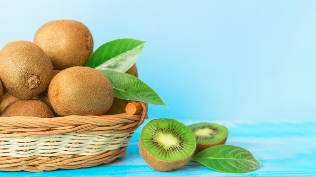 whole kiwi fruit in a wicker basket and kiwi halves on a blue background close-up. background with ripe kiwi fruit.