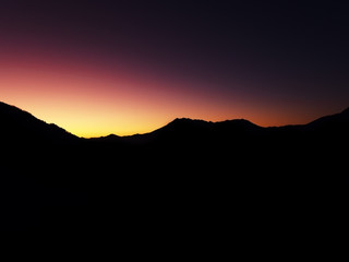View of the dark outlines of a mountain range against the backdrop of an iridescent red-yellow sunset sky