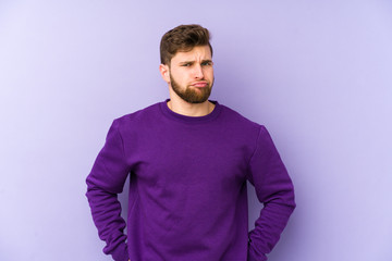 Young caucasian man isolated on purple background sad, serious face, feeling miserable and displeased.