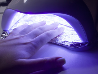 A woman dries gel polish on her nails in an ultraviolet lamp for manicure. UV lamp in a nail salon. Professional manicure.