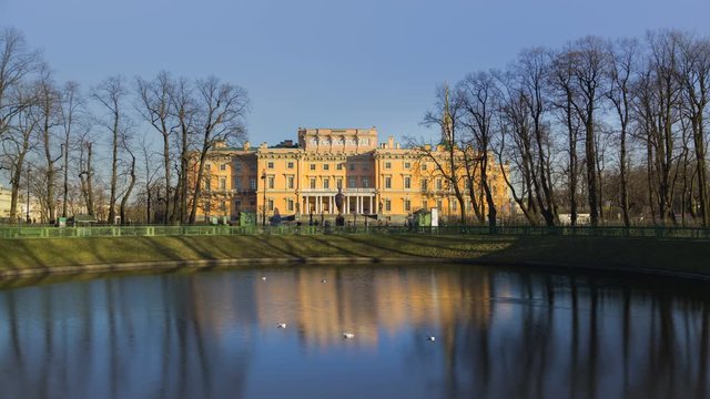 Timelapse of Engineer's Castle (Mikhailovsky Castle or St. Michael's Castle) view from the Summer Garden, people walk along the paths, spring, сlear cloudless sky, sunset, St. Petersburg, Russia