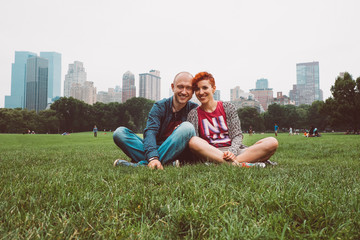 Happy couple enjoying romantic vacation outdoors in Central Park, New York City, USA. Smiling tourists man and woman in summer sun sitting on grass in Manhattan. Dating young couple happy in love.