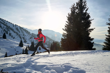 Trail runner in pink jacket woman running in winter mountains trail on snow.
