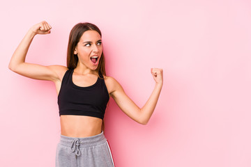 Young caucasian fitness woman posing in a pink background raising fist after a victory, winner...
