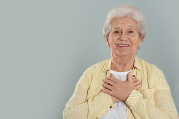 Grateful senior woman with hands on chest against grey background. Space for text