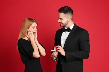 Man with engagement ring making marriage proposal to girlfriend on red background
