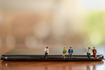 Business and Communication Cencept. Close up of group of businessman and woman miniature figure people sitting on smart mobile phone talking with newspaper with copy space.