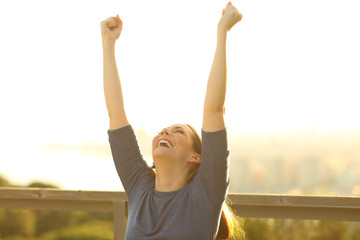 Excited woman raising arms at sunset in a park