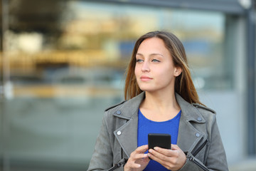 Confident entrepreneur holding phone looks at side