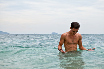 Young handsome man posing in water near ocean.