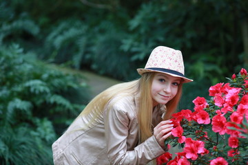 Young girl with long blond hair in a powdery jacket and a hat enjoys in the garden with blooming azalea