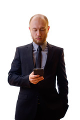 Businessman in a black suit, shirt and tie using a mobile phone in order to keep abreast of all the news. Makes the photo on the mobile phone, writes notes or new contacts and plays the game.