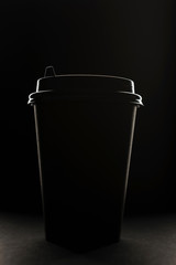 Black paper coffee cup on dark background. Silhouette of a black coffee cup on a black background.