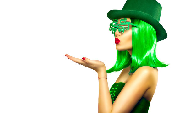St. Patrick's Day leprechaun model girl in green hat, funny clover sunglasses holding product, pointing hand, isolated on white background, kiss. Patrick Day pub party, celebrating. Green beer. Ads