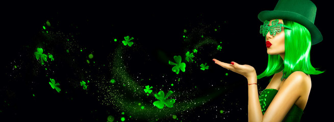 St. Patrick's Day leprechaun model girl pointing hand, holding product, isolated on black magic background, blowing shamrock leaves. Patrick Day pub party, celebrating. Border, Widescreen