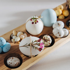Fototapeta na wymiar Natural Colored Eggs with flowers, easter chocolate eggs, candy and jelly bean in wooden egg box with sunlights. Stylish Compositions.