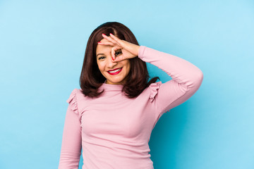 Middle age latin woman isolated excited keeping ok gesture on eye.